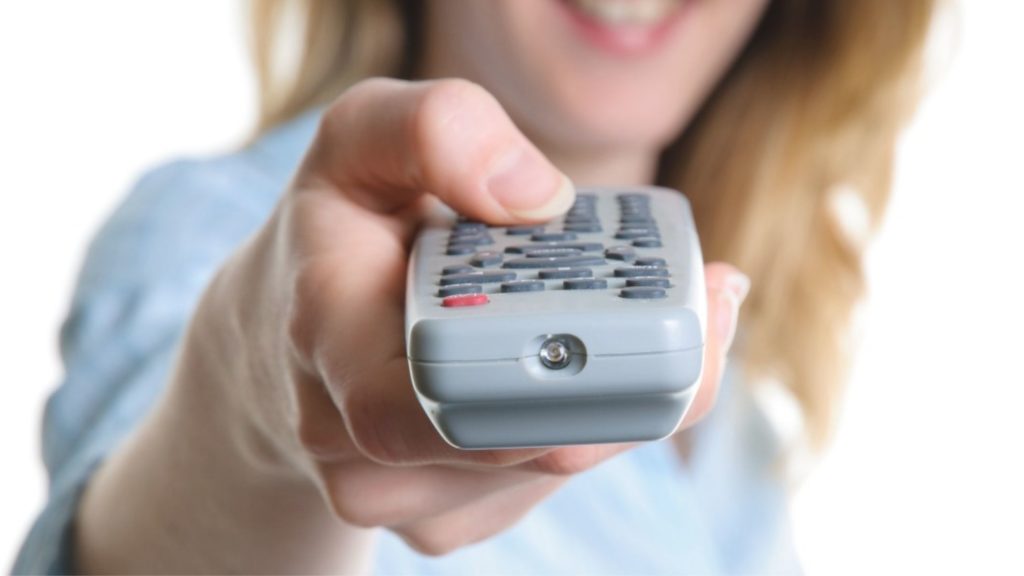 woman pressing pause button on remote control, illustrating the power of pause (The Power of the Pause for Introverted Leaders Wanting to Command the Room)