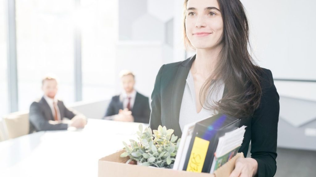 Woman resigning from her job and walking away, with smile on her face, from a meeting, with a box containing her belongings