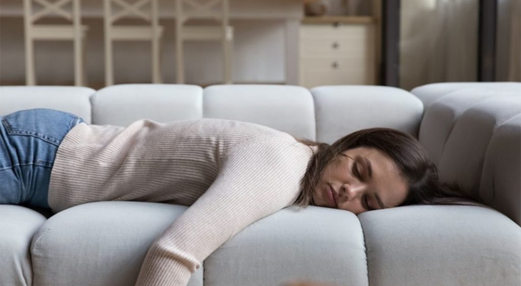 introverted female lying face down on couch at home, energy depleted by her work environment