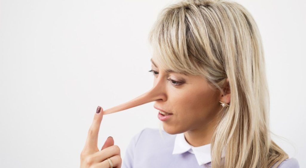 woman lying to herself as shown pointing to her pinocchio style extra long nose